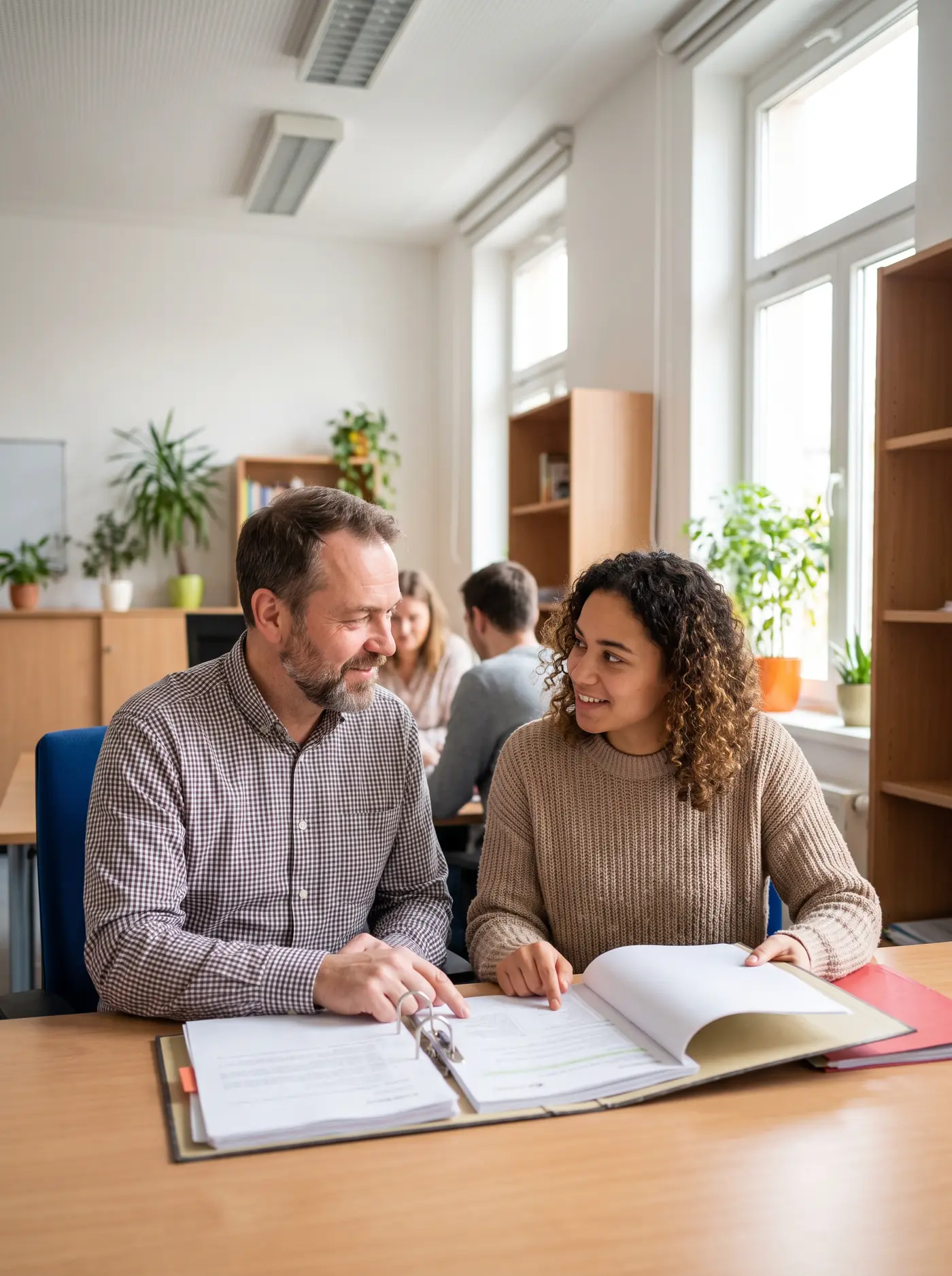 Zwei Mitarbeitende einer Einrichtung gehen am Schreibtisch Unterlagen durch